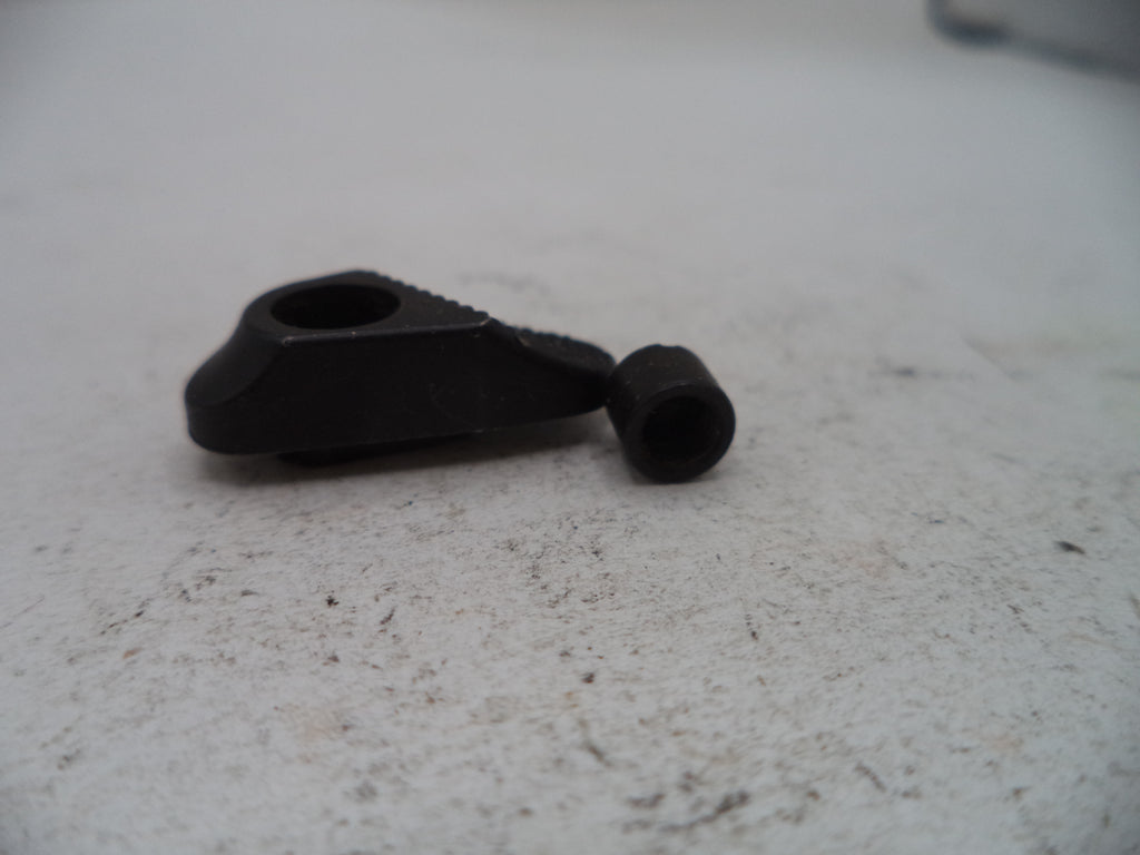 A small black plastic or metal hardware component with a triangular shape and a cylindrical hole, shown next to a matching small black cylindrical piece on a light gray textured surface.