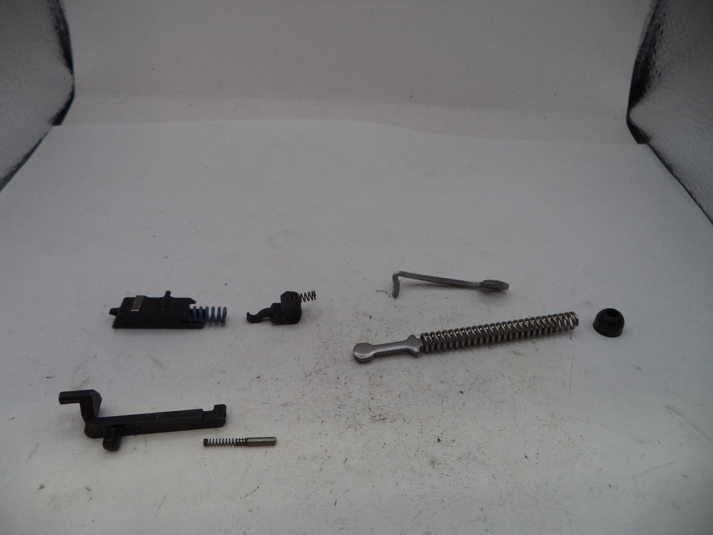 A set of disassembled metal and black mechanical parts, including springs, rods, and small hardware pieces, arranged on a white surface.