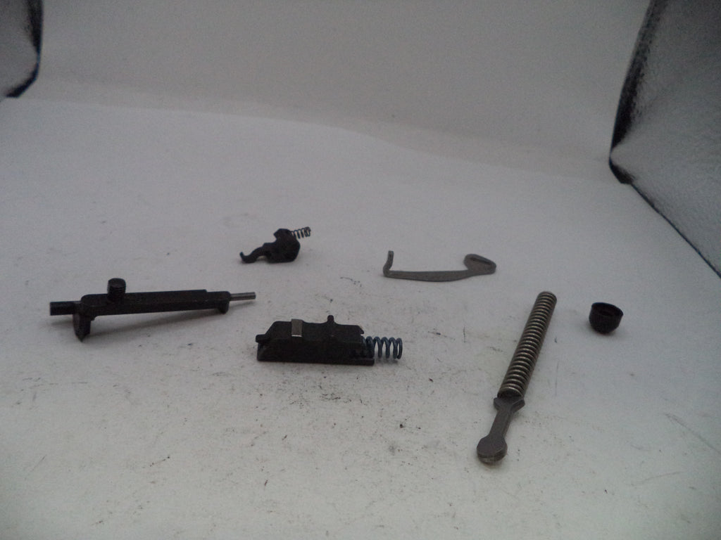 A set of disassembled black and silver metal mechanical parts, including a long rod, a spring, a small black cap, and other small hardware pieces, arranged on a white surface.