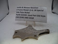 A used metal side plate for a Smith & Wesson revolver, displayed on a clear plastic stand with a paper label card behind it on a white surface.
