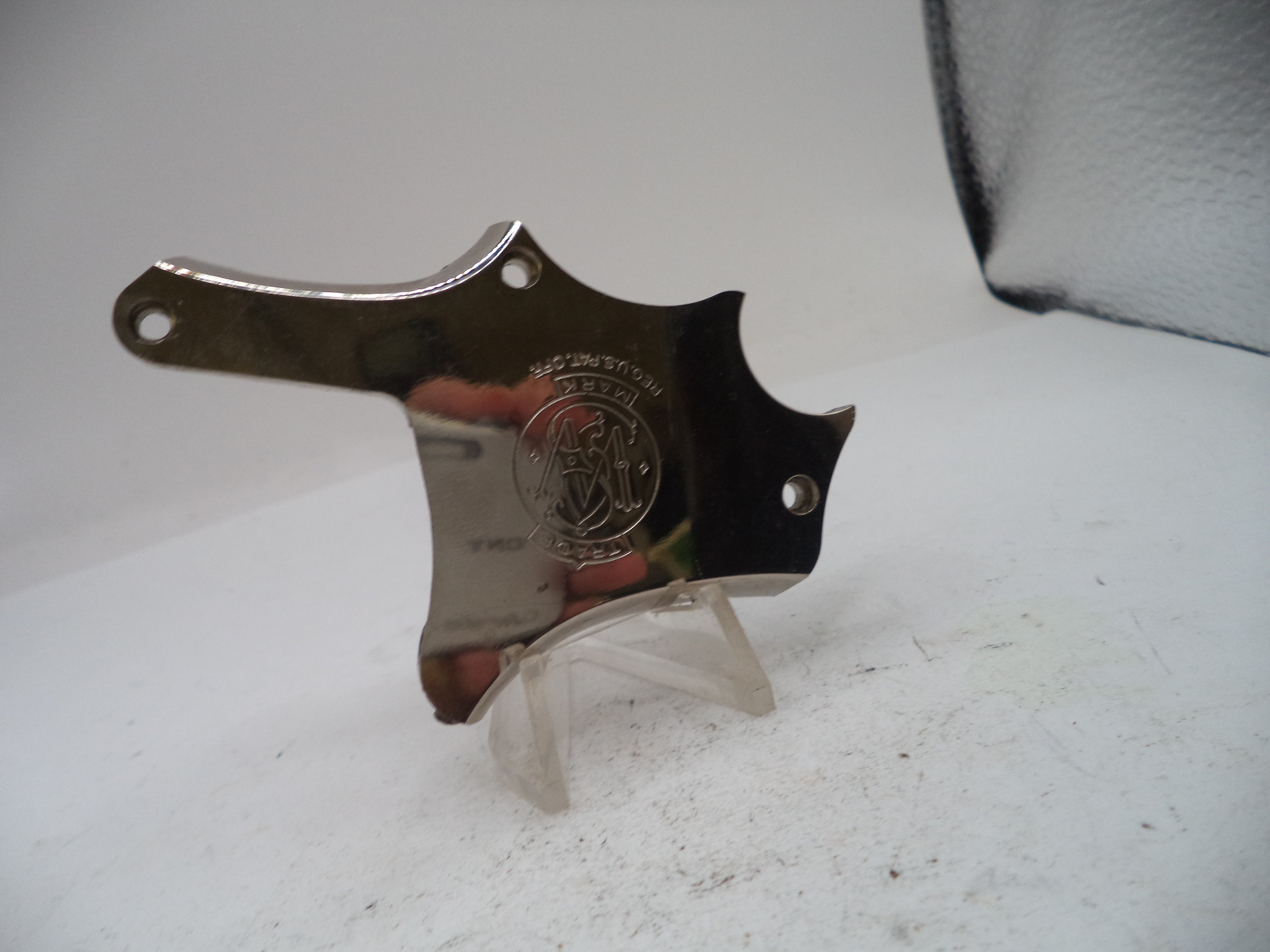 A polished silver metal knife guard with a circular engraved crest, displayed on a clear plastic stand against a white background.
