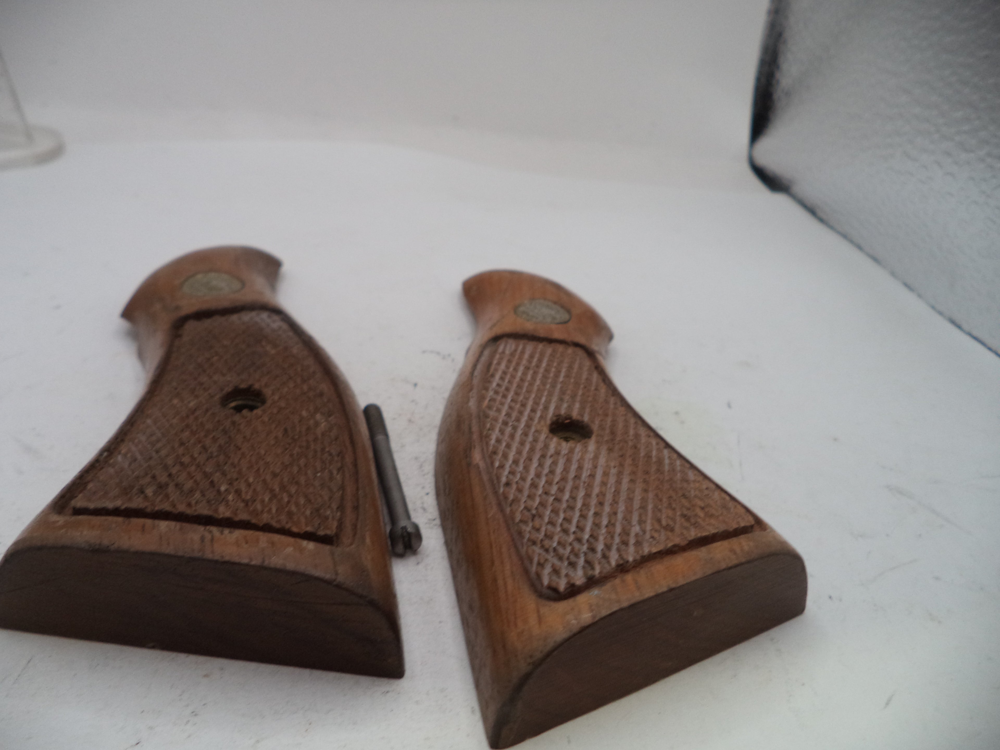 A pair of brown wooden grip covers with a textured checkered pattern and a small metal screw, displayed on a white surface.