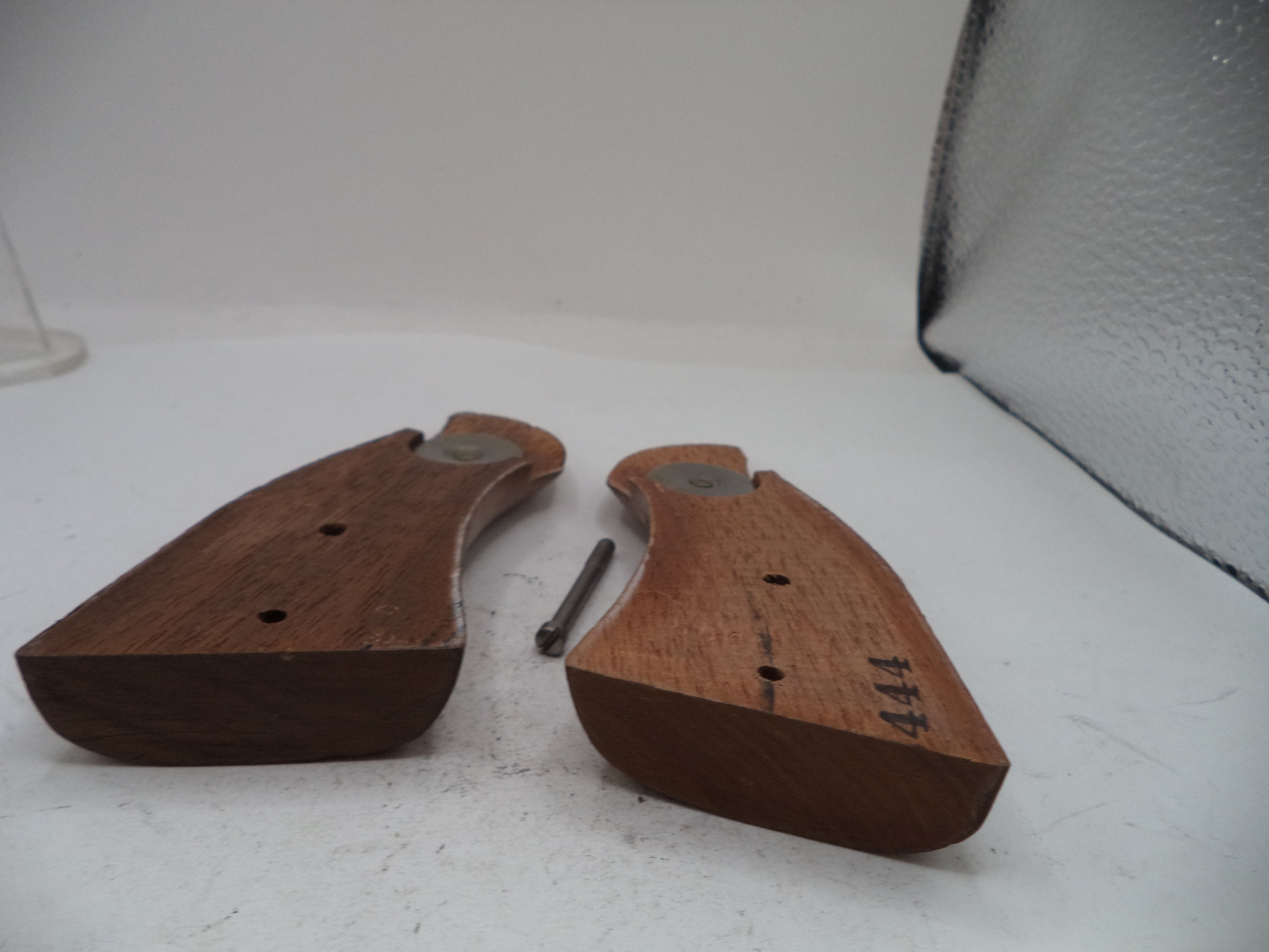 A pair of wooden gunstock grips with metal bolsters and a small metal pin, displayed on a white surface.