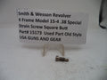 A small metal revolver strain screw part displayed on a clear plastic stand next to a paper label card that reads 'Smith & Wesson Revolver K Frame Model 15-4 .38 Special Strain Screw Square Butt Part# 15173 Used Part Old Style USA GUNS AND GEAR'.