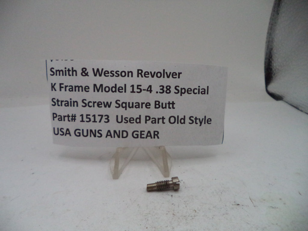 A small metal screw part displayed on a clear stand in front of a white sign that reads 'Smith & Wesson Revolver K Frame Model 15-4 .38 Special Strain Screw Square Butt Part# 15173 Used Part Old Style USA GUNS AND GEAR'.