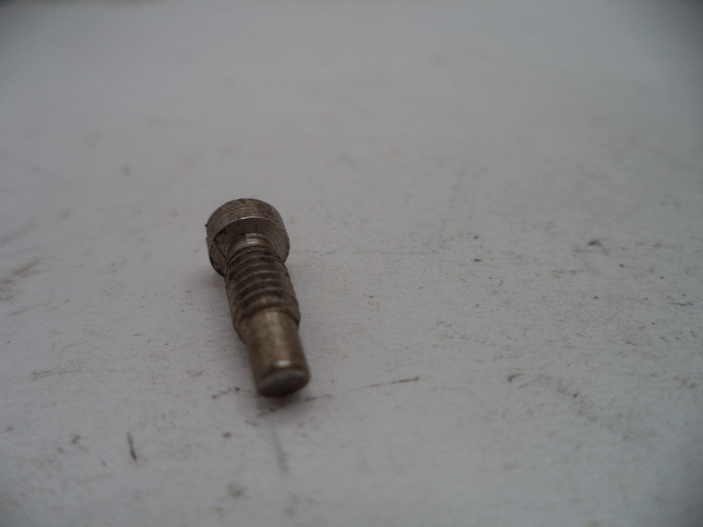 A small used metal threaded bolt or screw with a hex head, resting on a light gray textured surface.