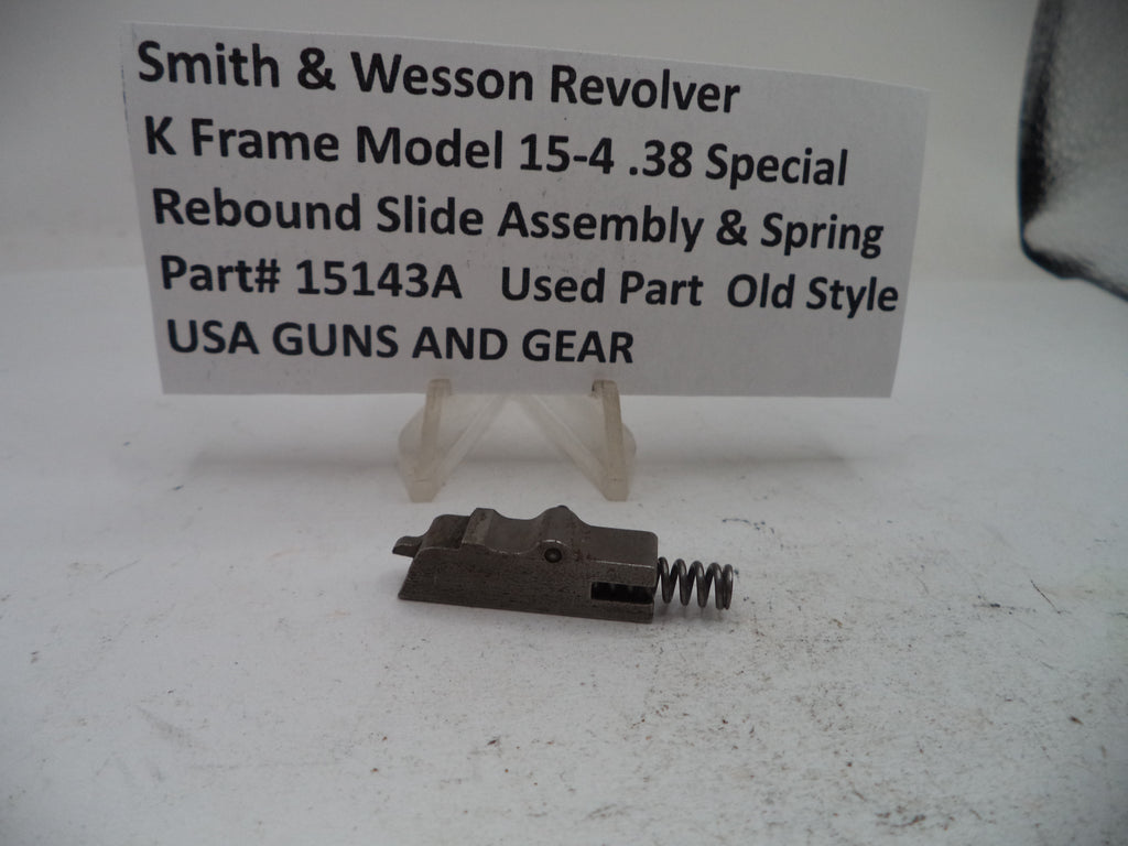 A metal revolver rebound slide assembly with a coil spring, displayed on a small clear stand in front of a white sign that reads 'Smith & Wesson Revolver K Frame Model 15-4 .38 Special Rebound Slide Assembly & Spring Part# 15143A Used Part Old Style USA GUNS AND GEAR'.