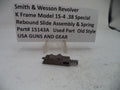 A metal revolver rebound slide assembly with a coil spring, displayed on a small clear stand in front of a white sign that reads 'Smith & Wesson Revolver K Frame Model 15-4 .38 Special Rebound Slide Assembly & Spring Part# 15143A Used Part Old Style USA GUNS AND GEAR'.