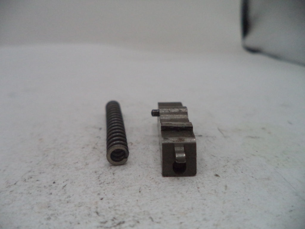 A small metal mechanical component and a dark metal spring placed on a light gray textured surface.