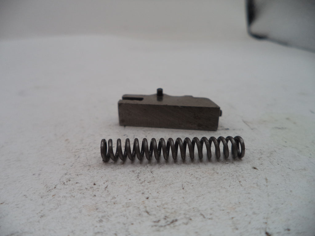 A small metal mechanical component and a coiled spring placed on a light gray textured surface.