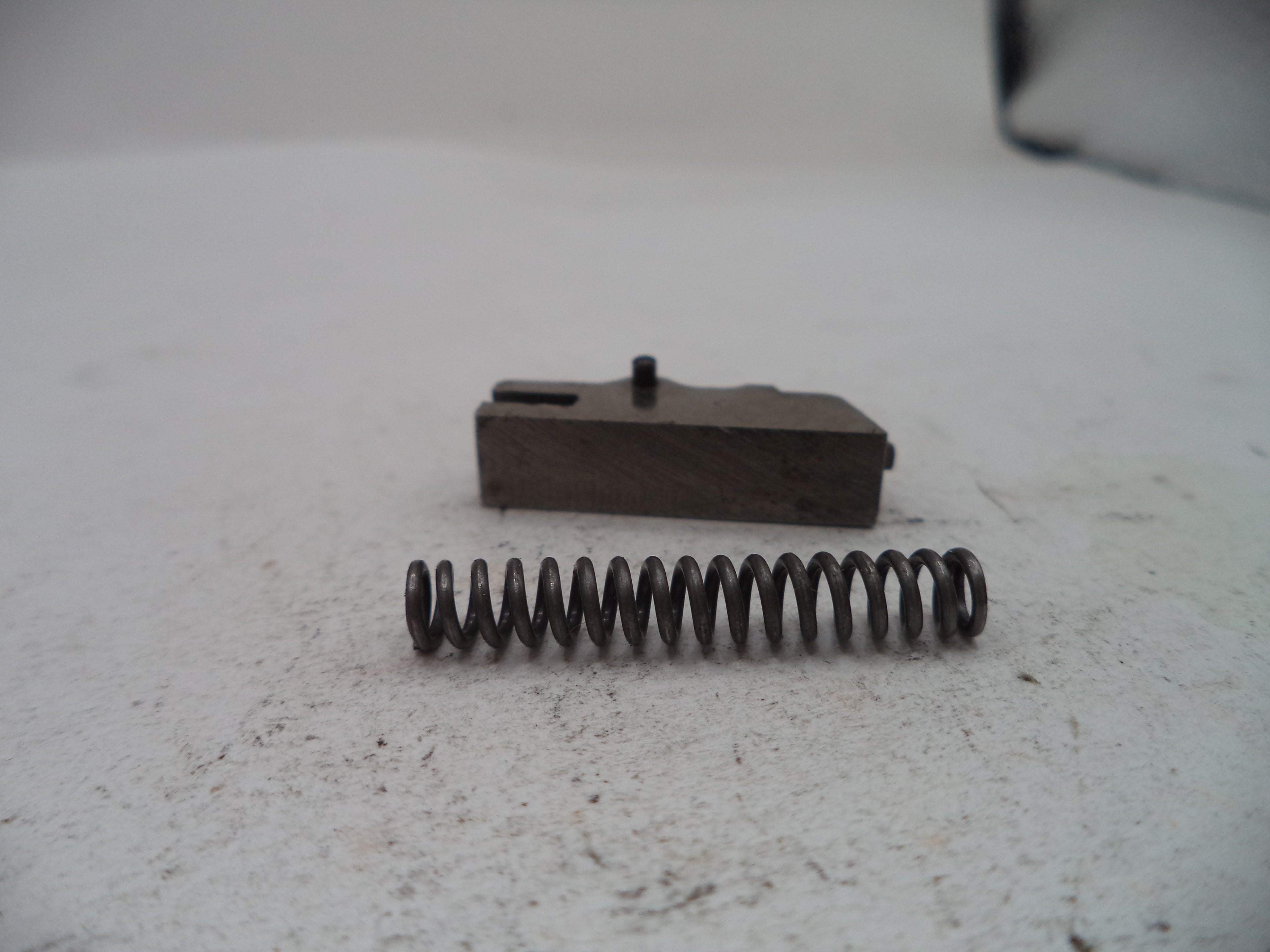 A small metal mechanical component and a coiled spring placed on a light gray textured surface.