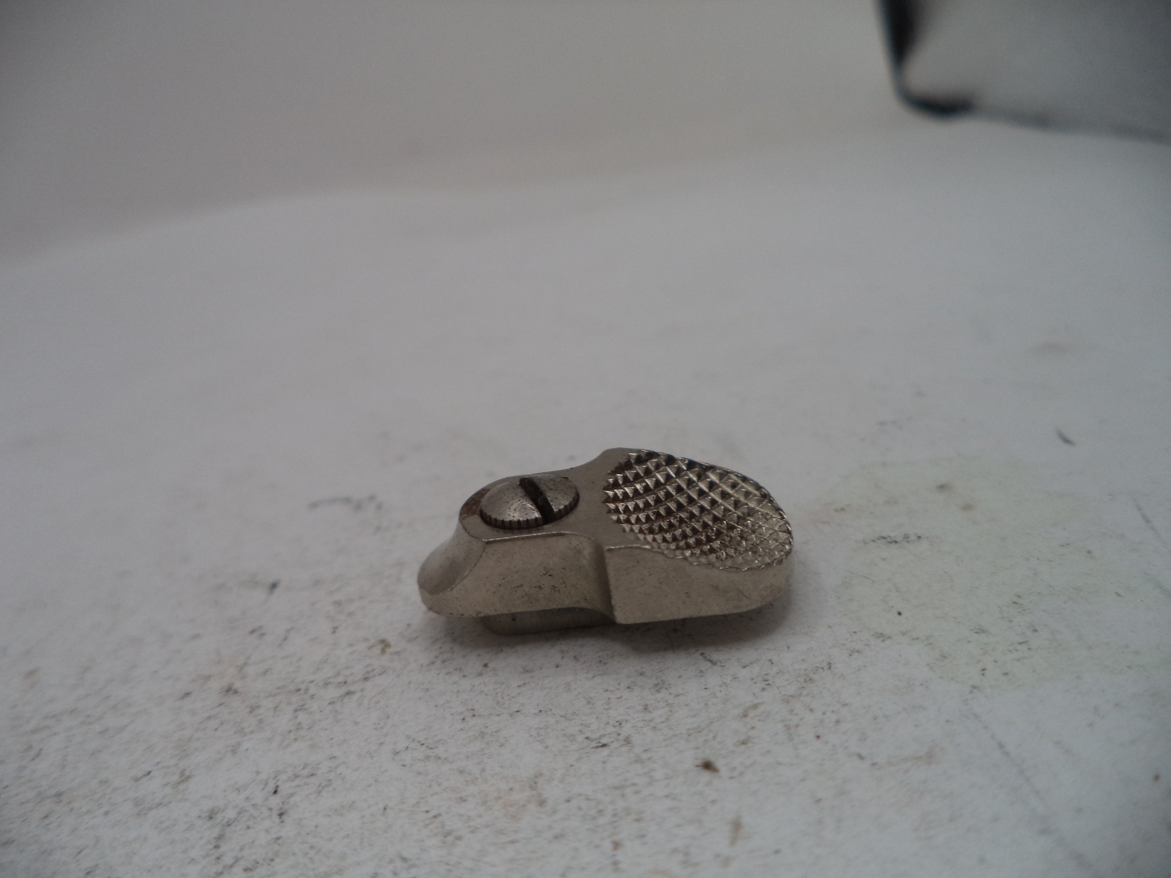 A small silver-colored metal mechanical part with a textured mesh surface and a screw, resting on a light gray surface.