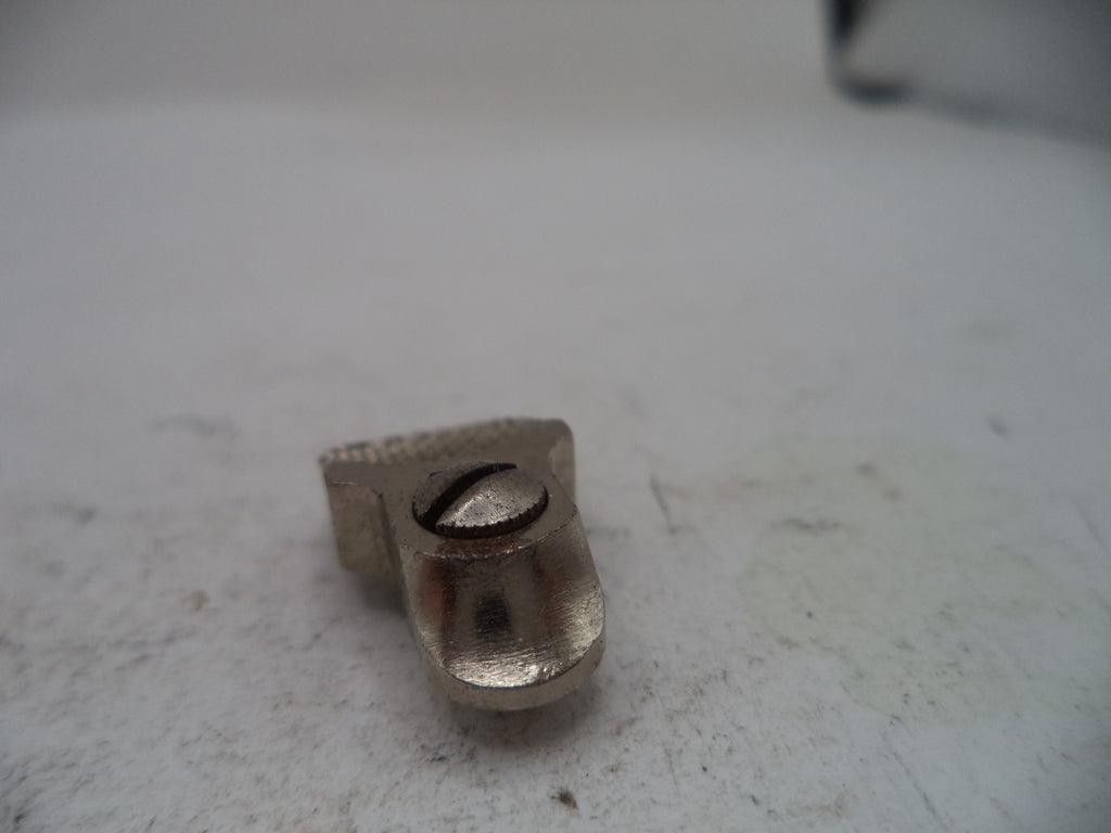 A small metallic silver hardware component, possibly a bracket or mounting piece, photographed on a worn off-white surface.