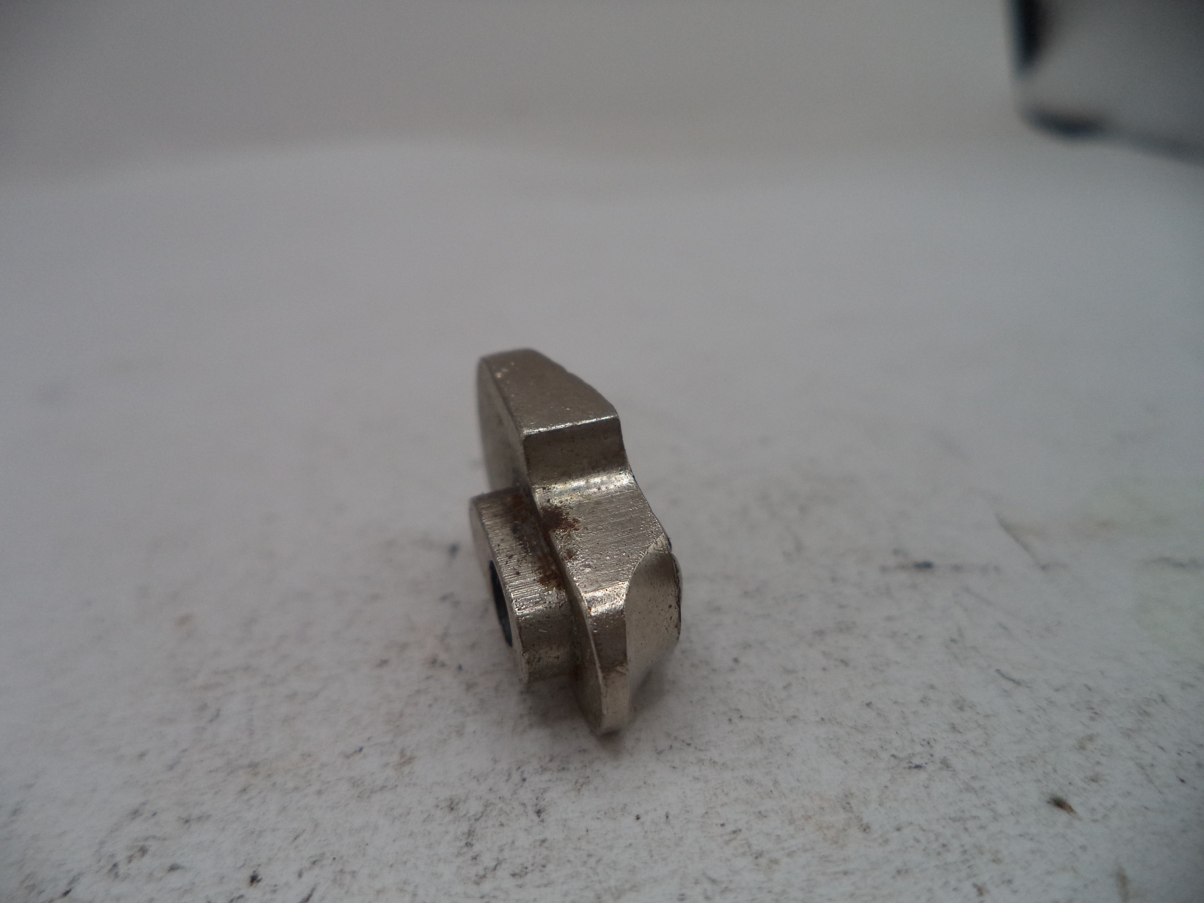 A small metallic silver hardware component, possibly a machined bolt head or spacer, resting on a textured off-white surface.