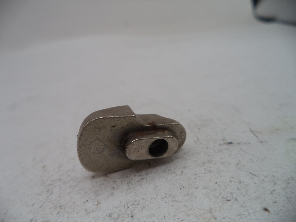 A small metallic mechanical component, possibly a bracket or clip, with a central hole, resting on a textured off-white surface.