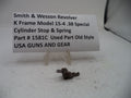 A small metal cylinder stop and spring part displayed on a white surface in front of a white sign that reads 'Smith & Wesson Revolver K Frame Model 15-4 .38 Special Cylinder Stop & Spring Part # 1581C Used Part Old Style USA GUNS AND GEAR'.
