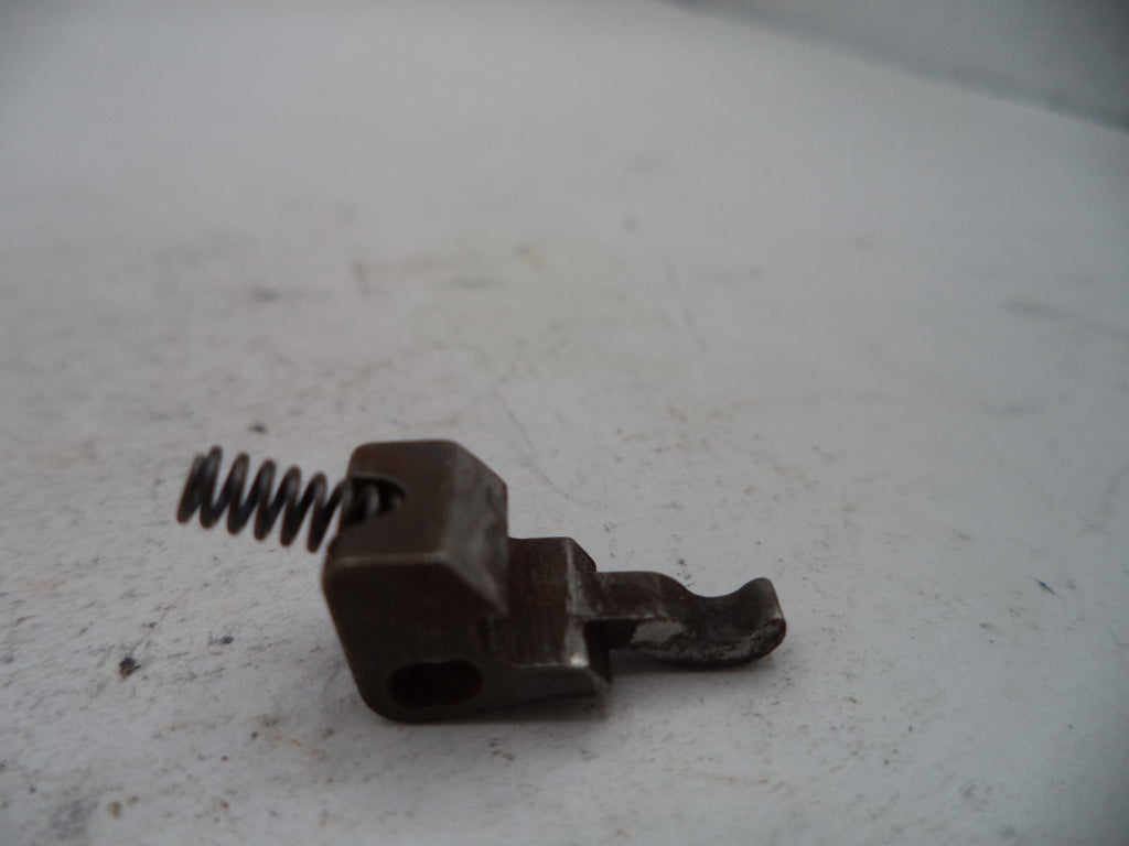 A small dark metal mechanical component with a coiled spring, photographed on a light gray surface.