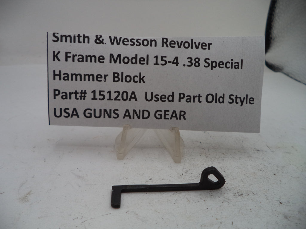 A small black metal hammer block part displayed on a clear stand in front of a printed label that reads 'Smith & Wesson Revolver K Frame Model 15-4.38 Special Hammer Block Part# 15120A Used Part Old Style USA GUNS AND GEAR'.