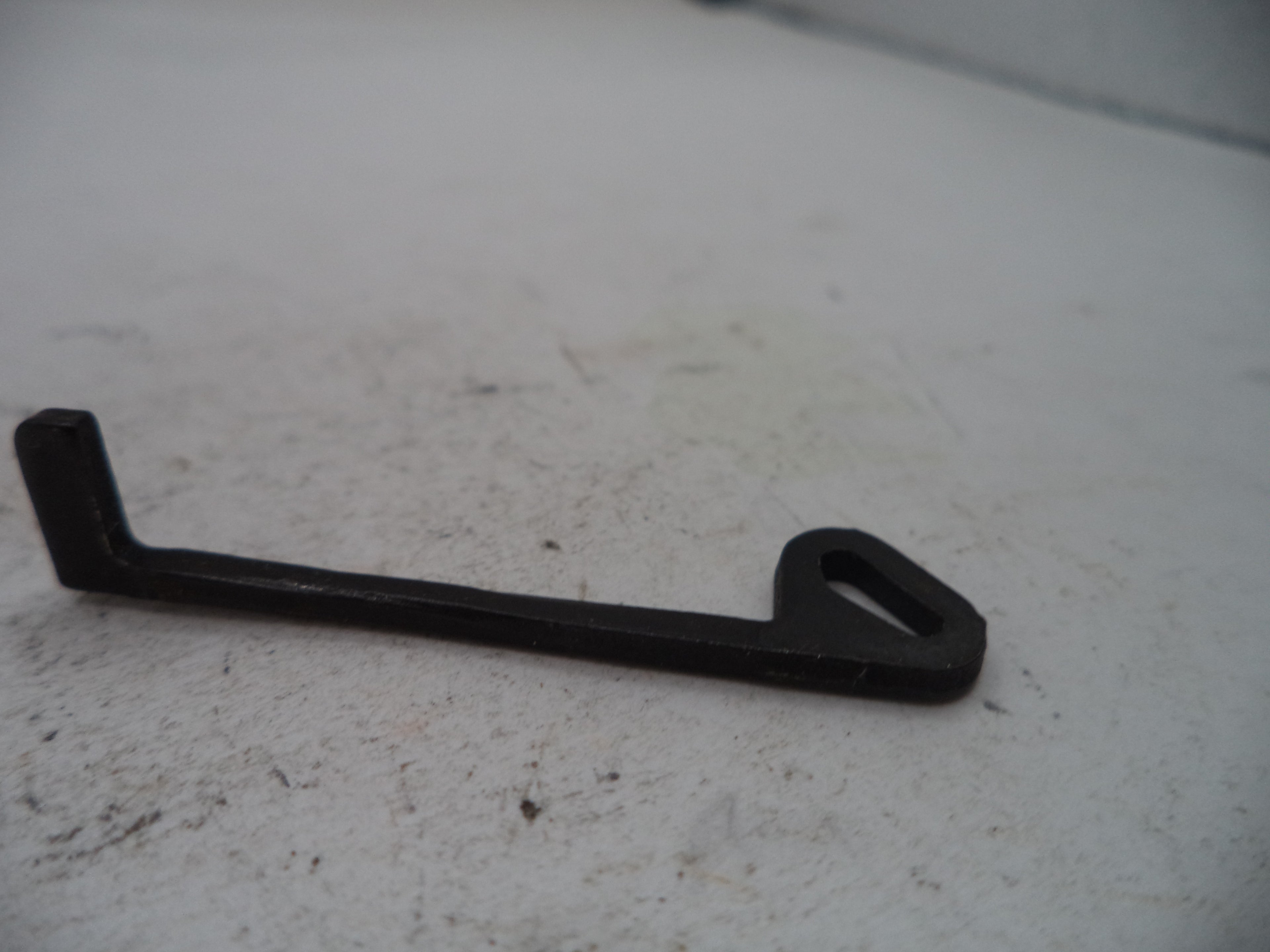 A small black metal bracket or hook with a triangular cutout at one end, photographed on a light gray textured surface.