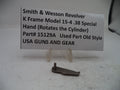 A small metal revolver part labeled 'Smith & Wesson Revolver K Frame Model 15-4 .38 Special Hand (Rotates the Cylinder)' on a white display stand in front of a paper sign.