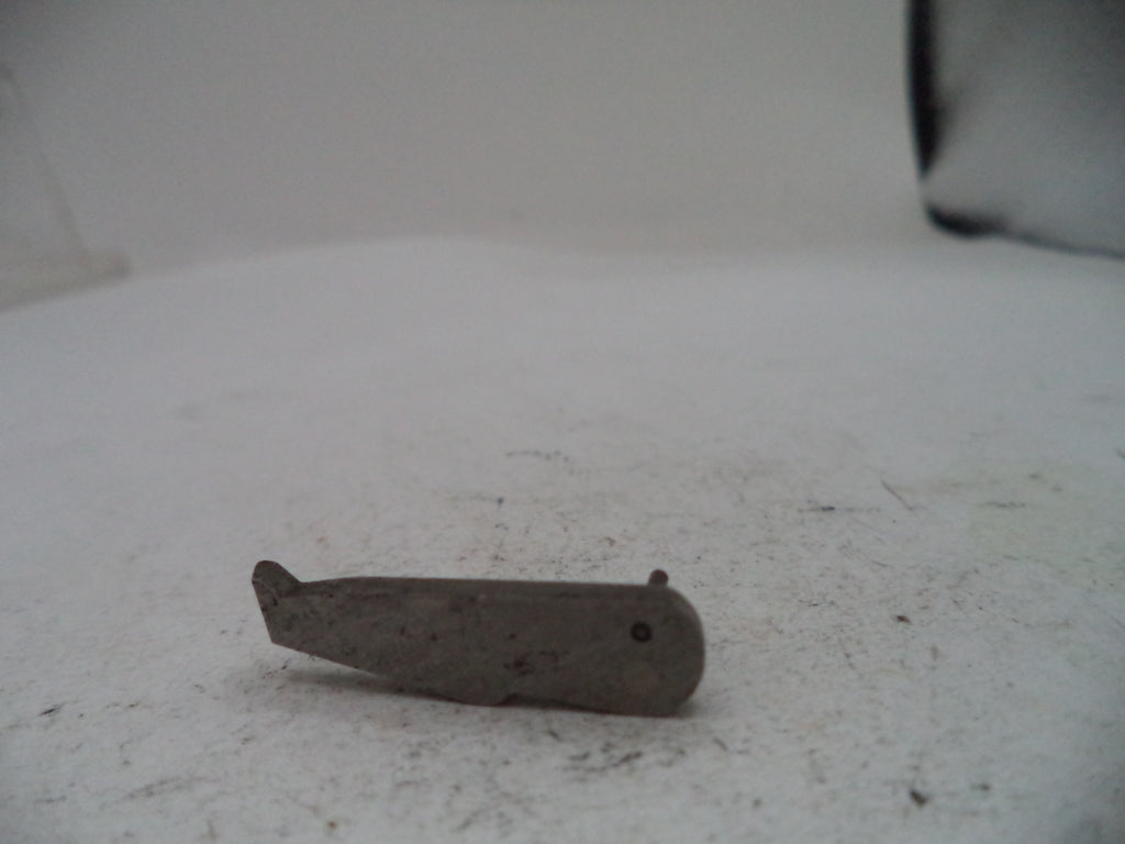 A small, worn metal tool or hardware piece with a dark, weathered finish, resting on a dusty white surface.