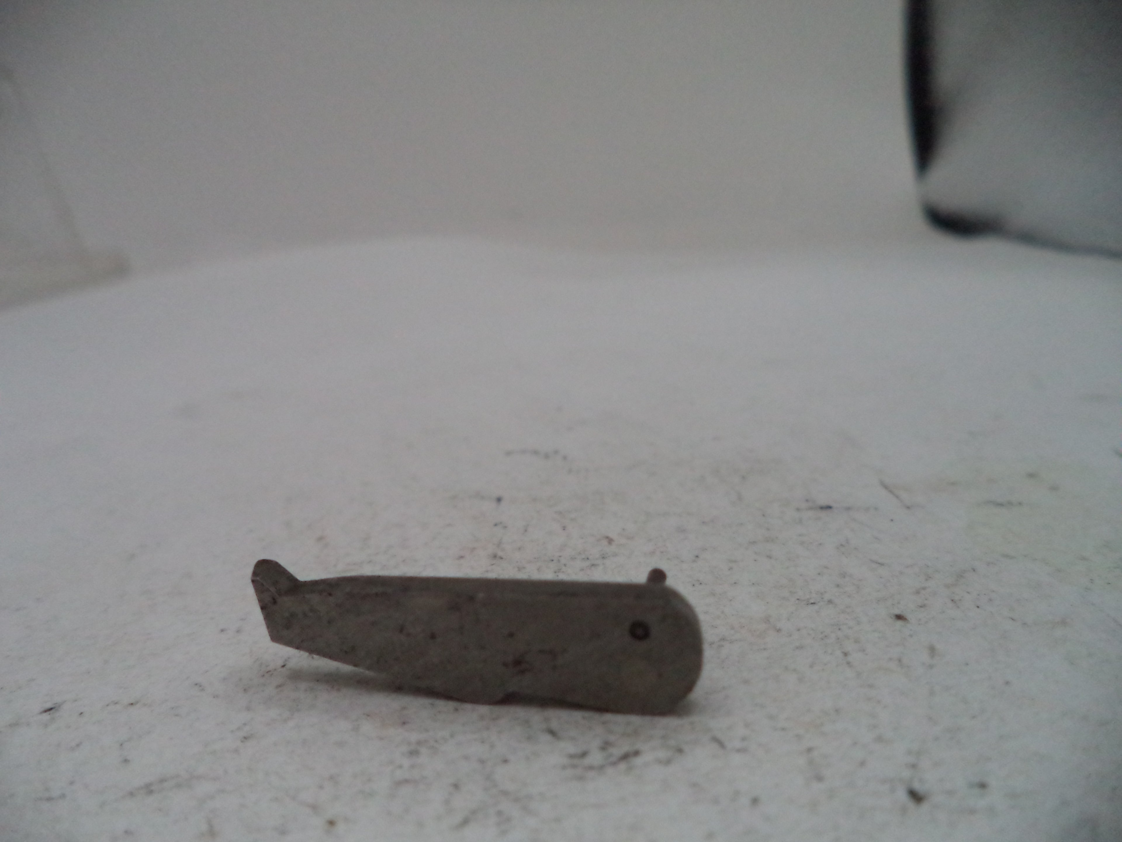 A small, worn metal tool or hardware piece with a dark, weathered finish, resting on a dusty white surface.