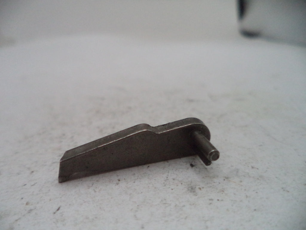 A small dark metal mechanical part or pin with a flat angled body and a protruding cylindrical pin, photographed on a light gray surface.