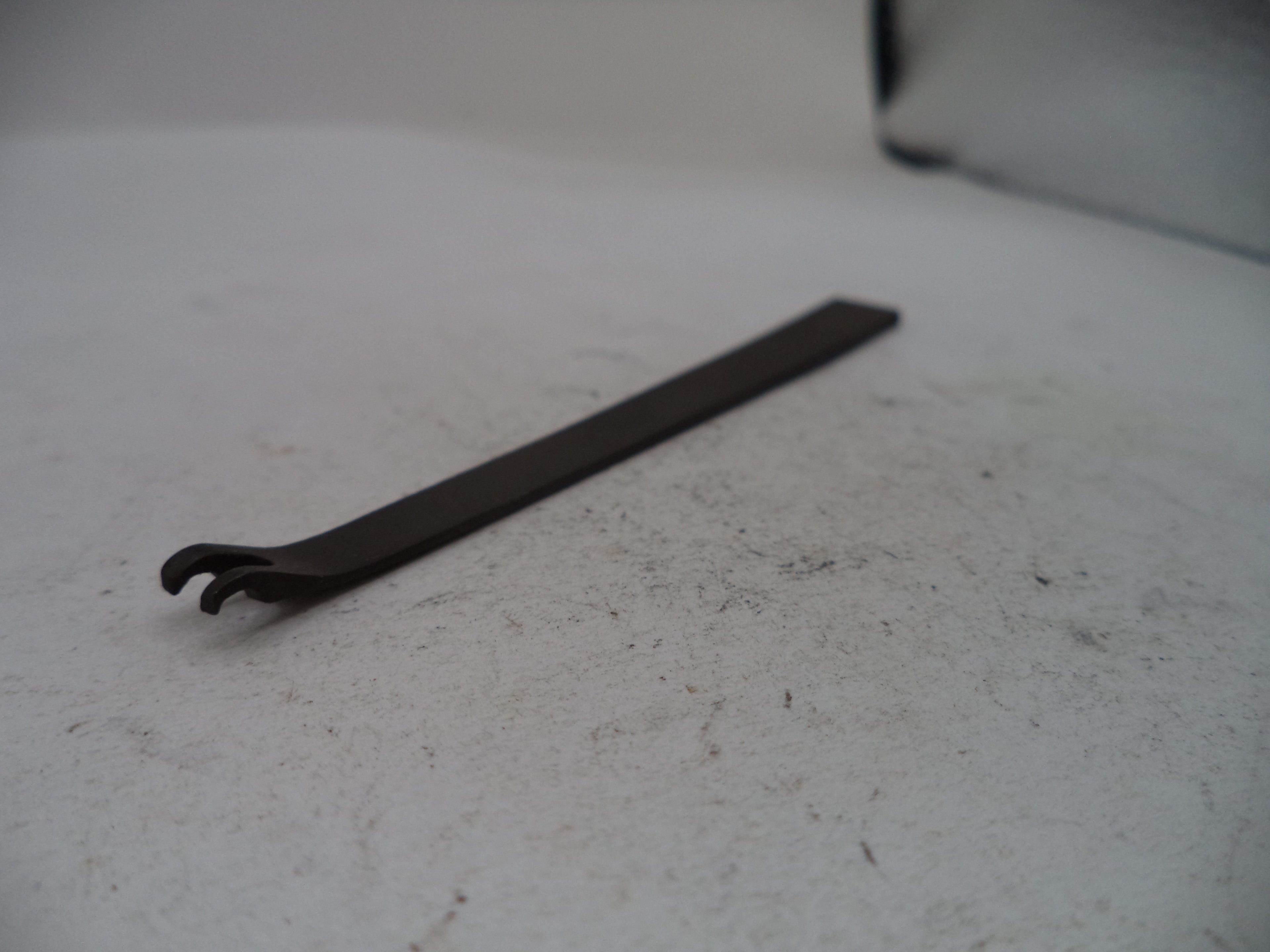 A dark metal flathead screwdriver with a claw-like tip, resting on a textured off-white surface.