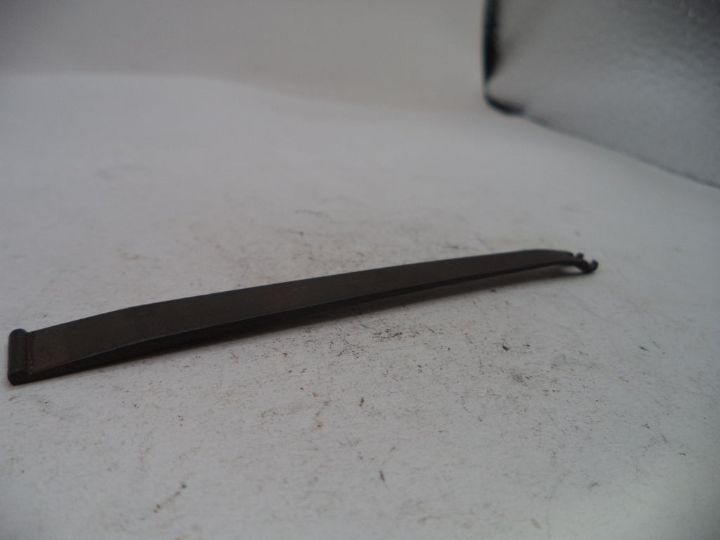 A long, thin black metal tool with a flat blade and a small hook-like end, photographed on a light gray surface.