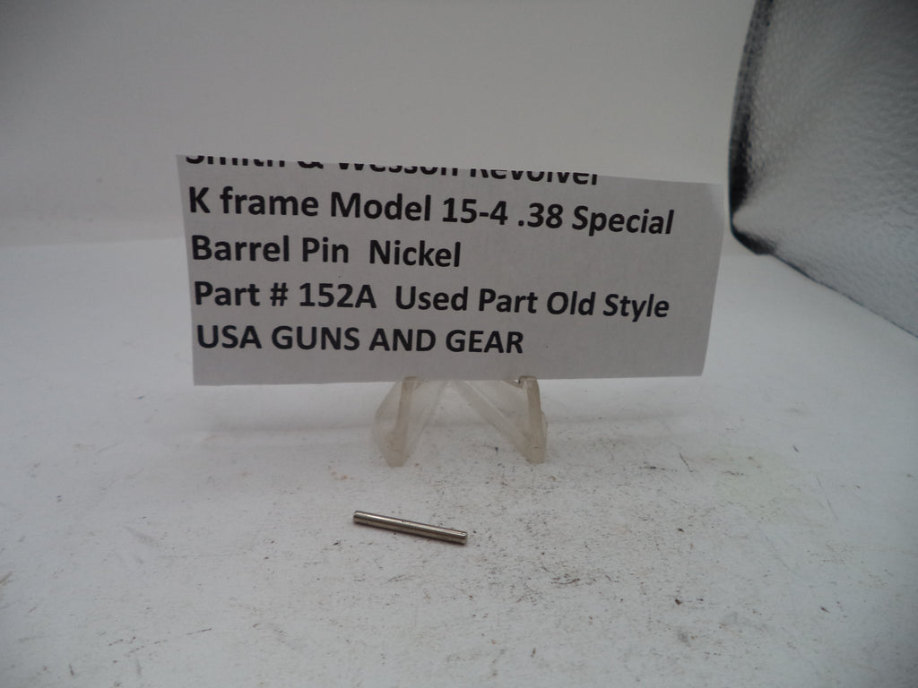 A small metallic nickel barrel pin displayed on a white surface next to a paper label that reads 'Smith & Wesson Revolver K frame Model 15-4 .38 Special Barrel Pin Nickel Part # 152A Used Part Old Style USA GUNS AND GEAR'.