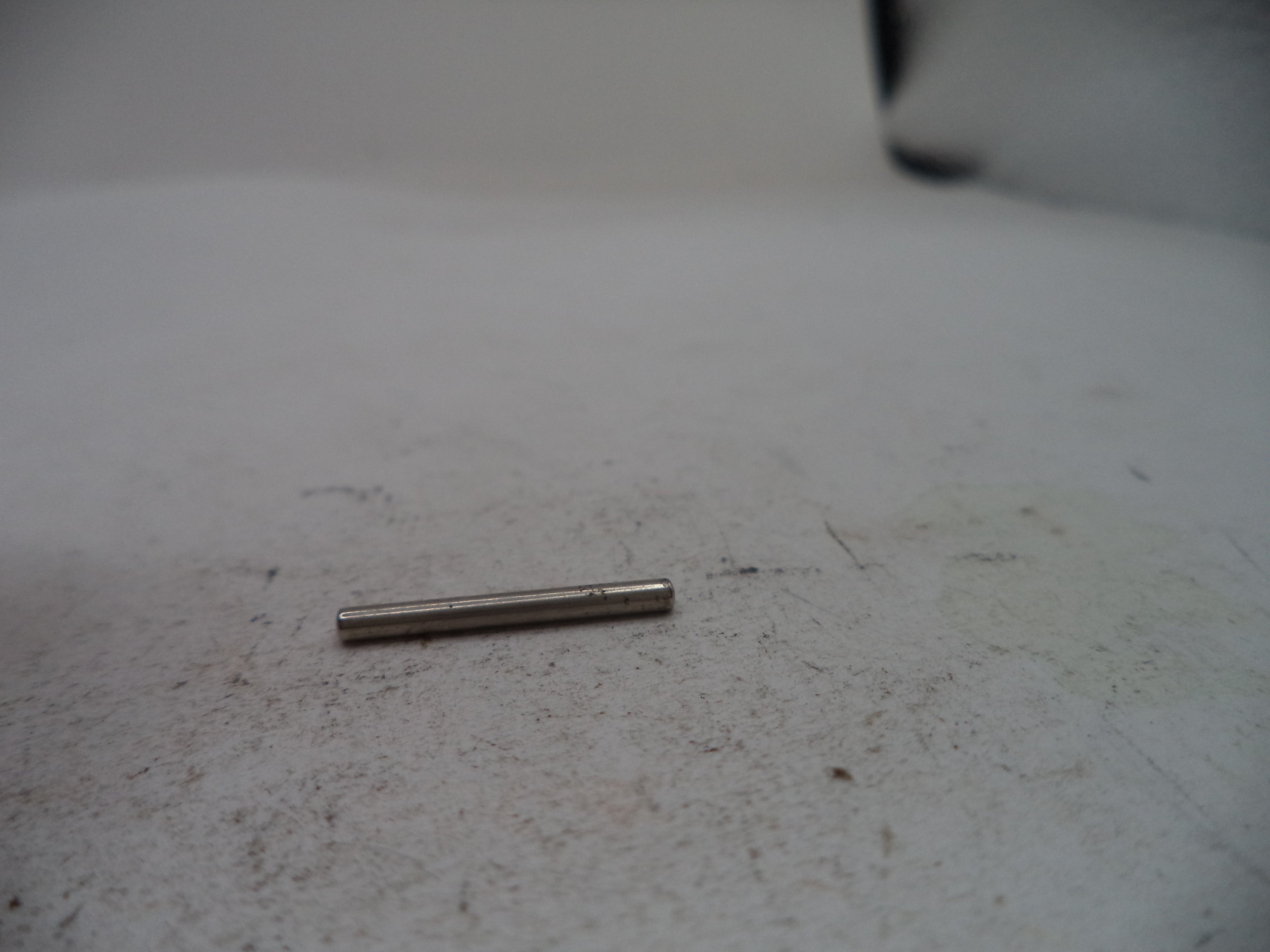 A small metallic cylindrical pin or rod lying on a dirty off-white surface.