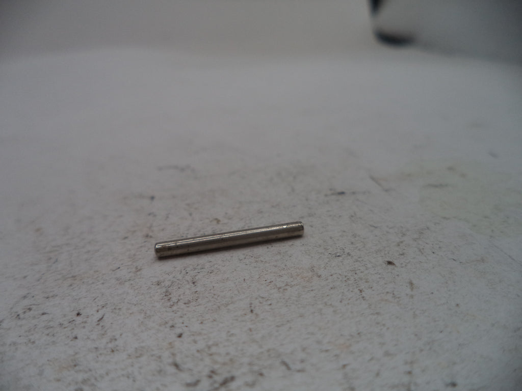 A small metallic cylindrical pin or rod lying on a light gray textured surface.