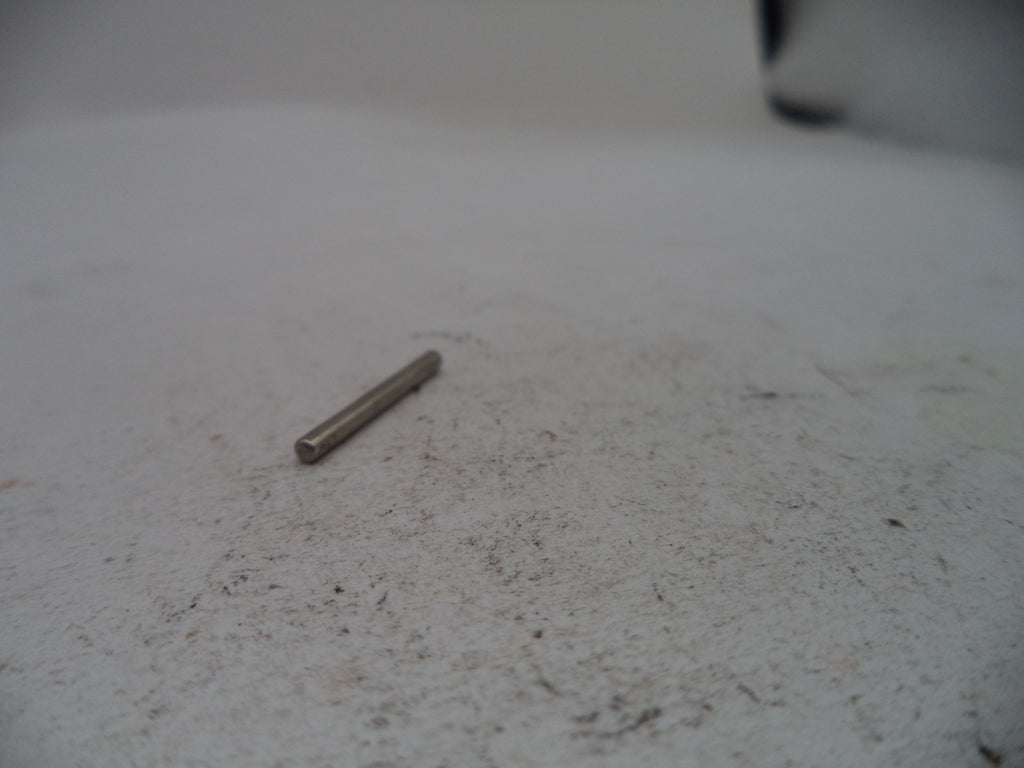 A small metallic cylindrical pin or rod lying on a light gray textured surface.