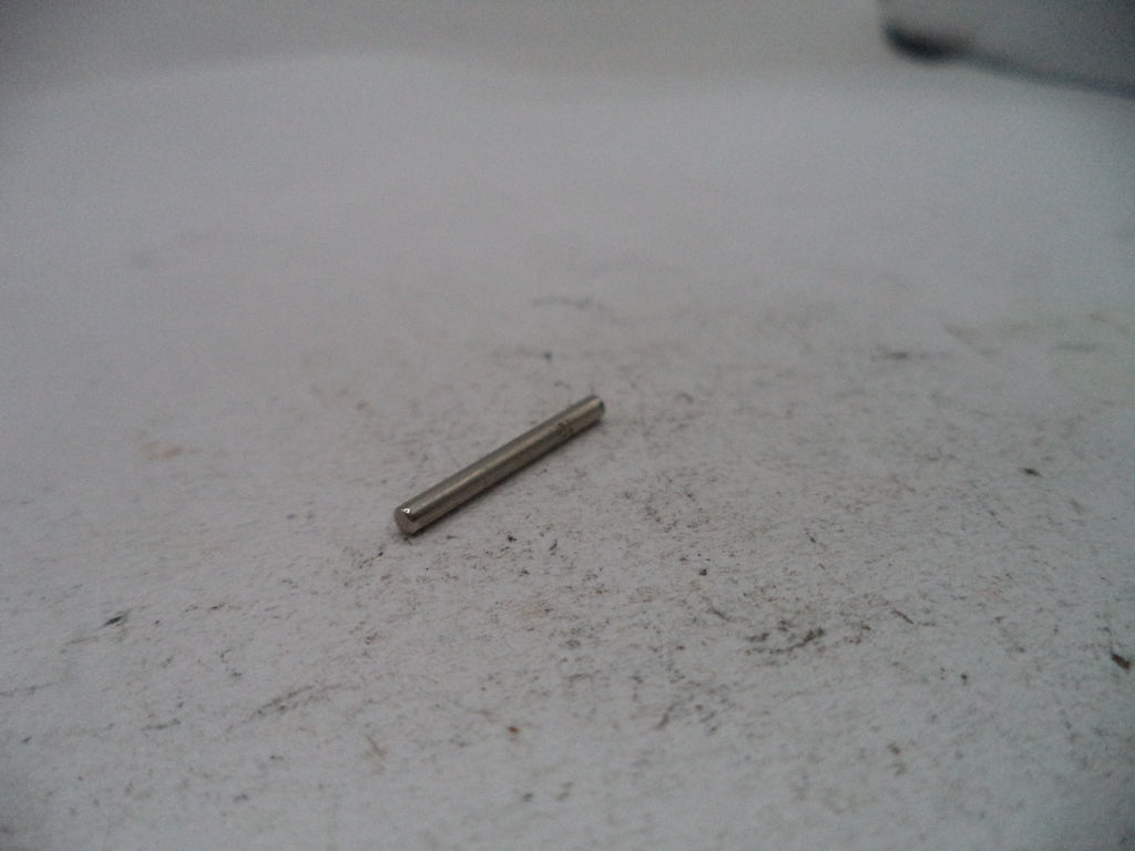 A small metallic cylindrical pin or rod lying on a light gray textured surface.