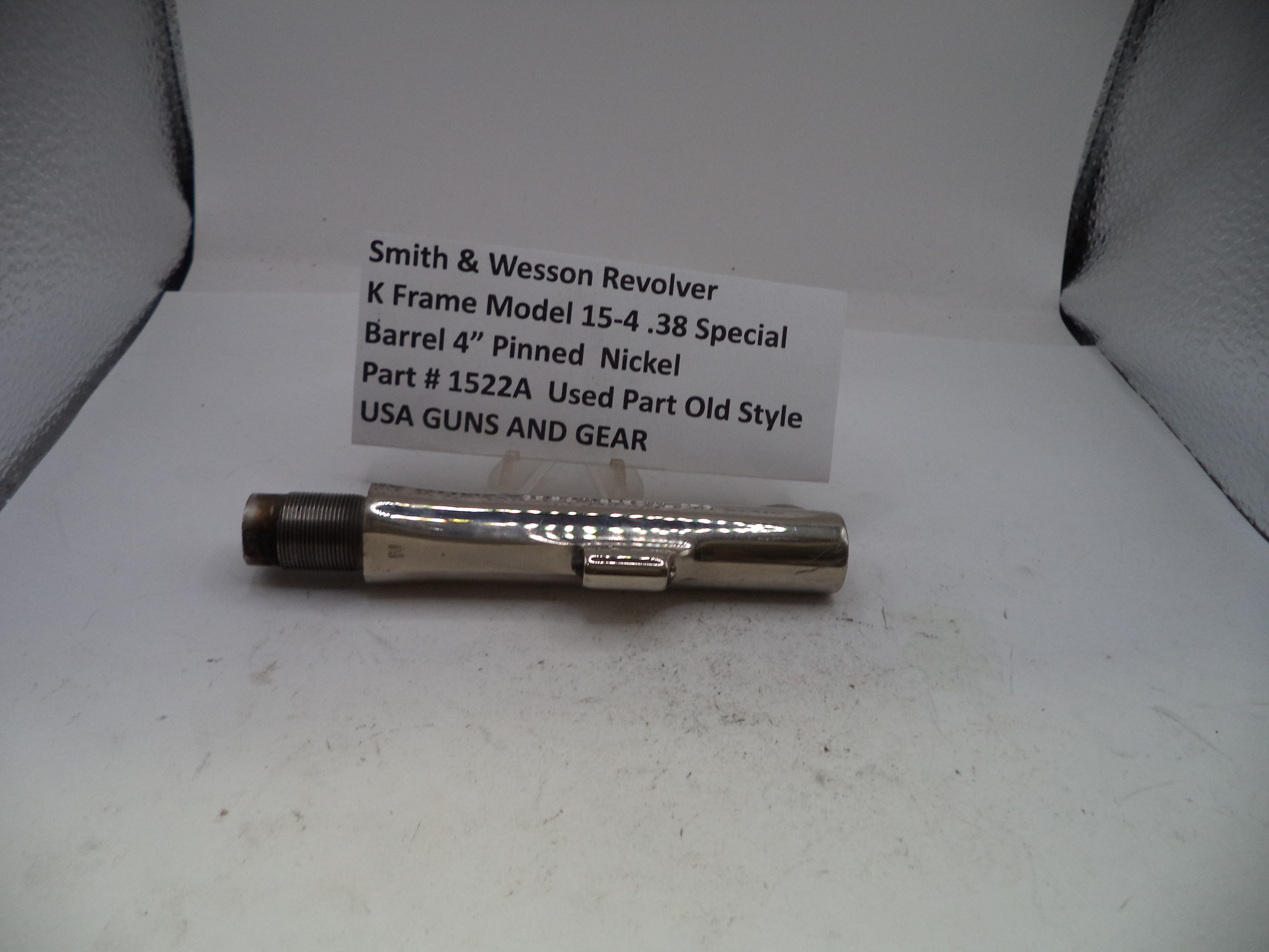 A used metal barrel component for a Smith & Wesson revolver, displayed on a white surface with a handwritten label card behind it.