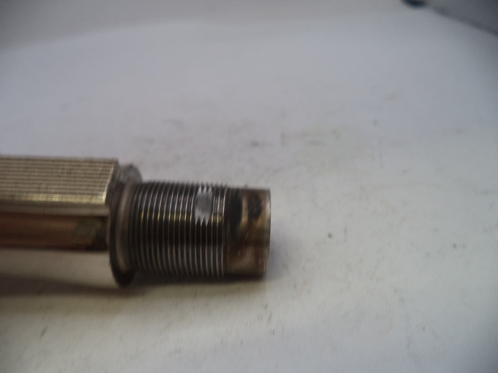 A close-up of a used metal threaded component, possibly a mechanical part or tool shank, showing a hex nut and a threaded section with rust and wear on a white surface.