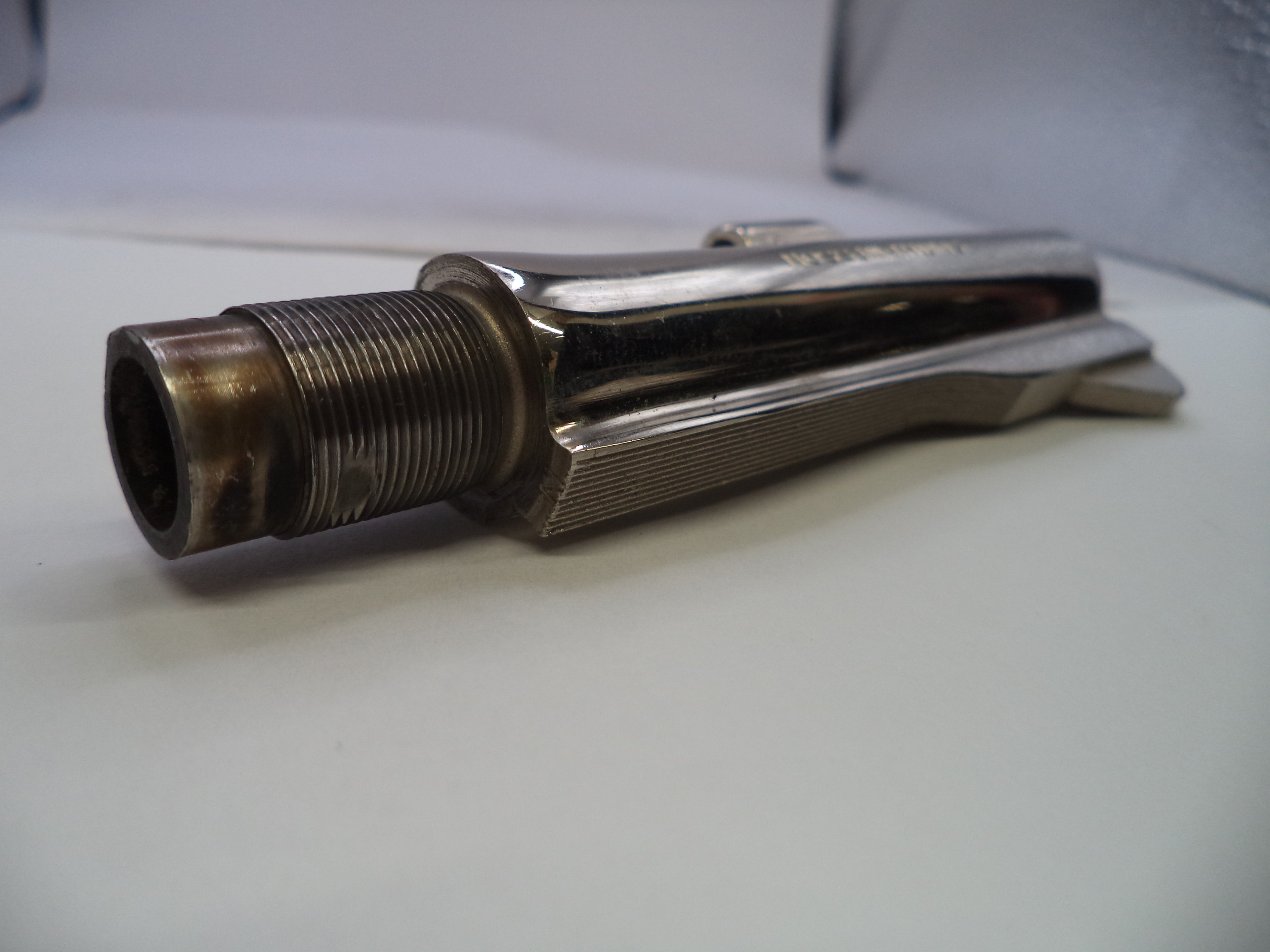 A vintage metallic bicycle fork, likely from a Harley-Davidson or similar cruiser motorcycle, featuring a threaded tube on one end and a polished chrome splined handlebar interface on the other, resting on a white surface.
