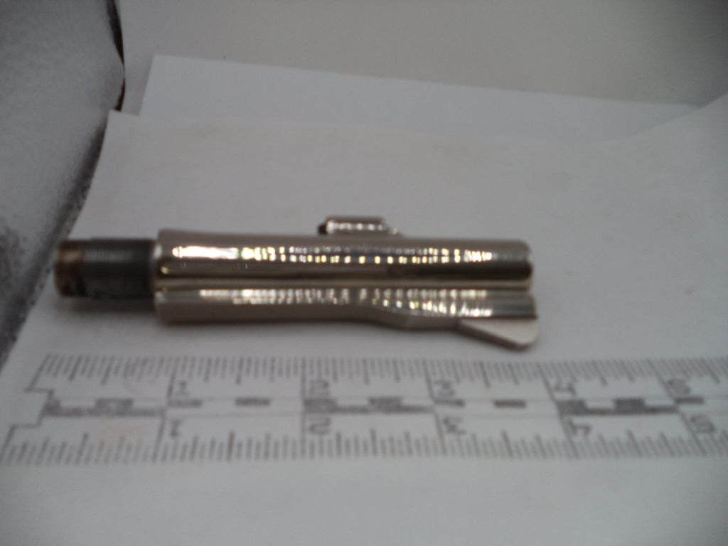 A small metallic cylindrical tool or accessory with a dark cap, resting on white paper above a ruler for scale.