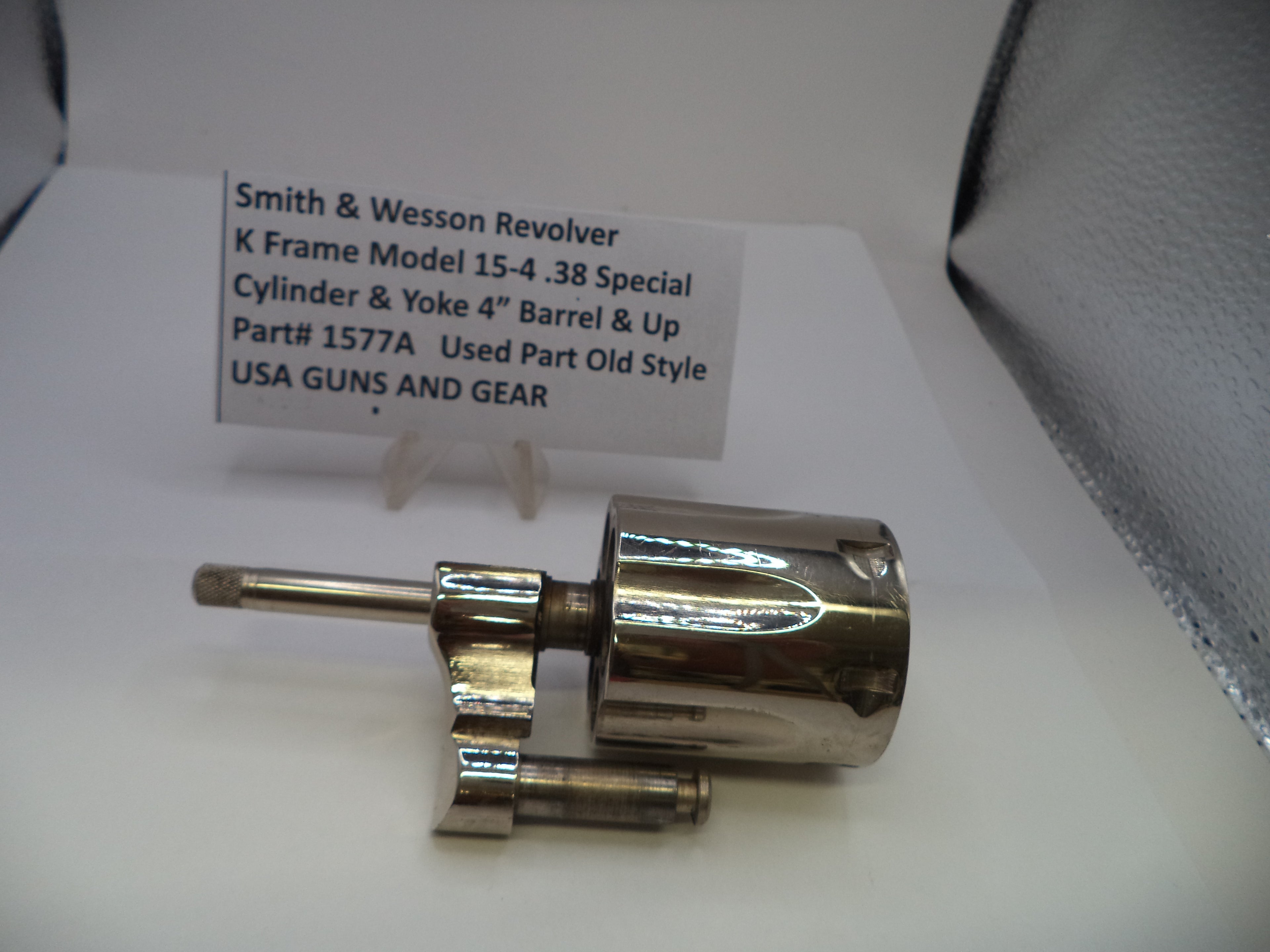 A polished metal Smith & Wesson revolver cylinder and yoke barrel replacement part, displayed on a white surface with a product information card behind it.