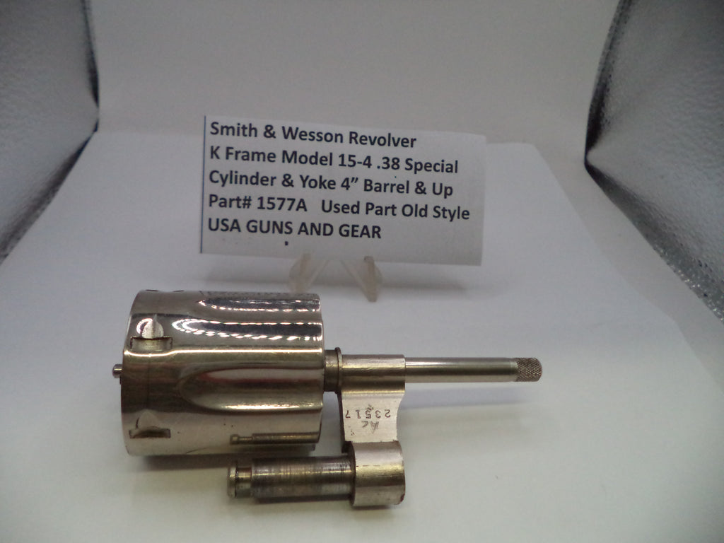 A metallic Smith & Wesson revolver cylinder and yoke part displayed on a white surface with a handwritten identification card behind it.