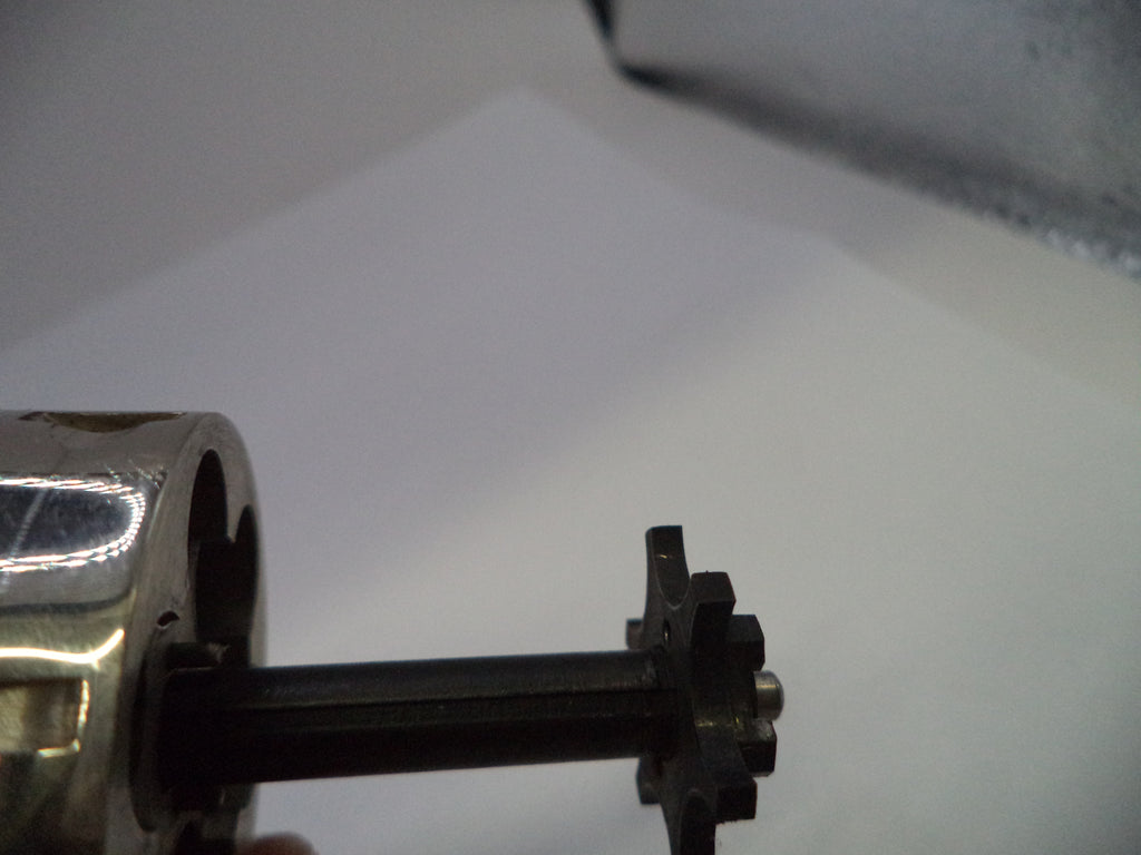 A close-up of a mechanical component featuring a black metal gear meshing with a silver metallic shaft and housing.