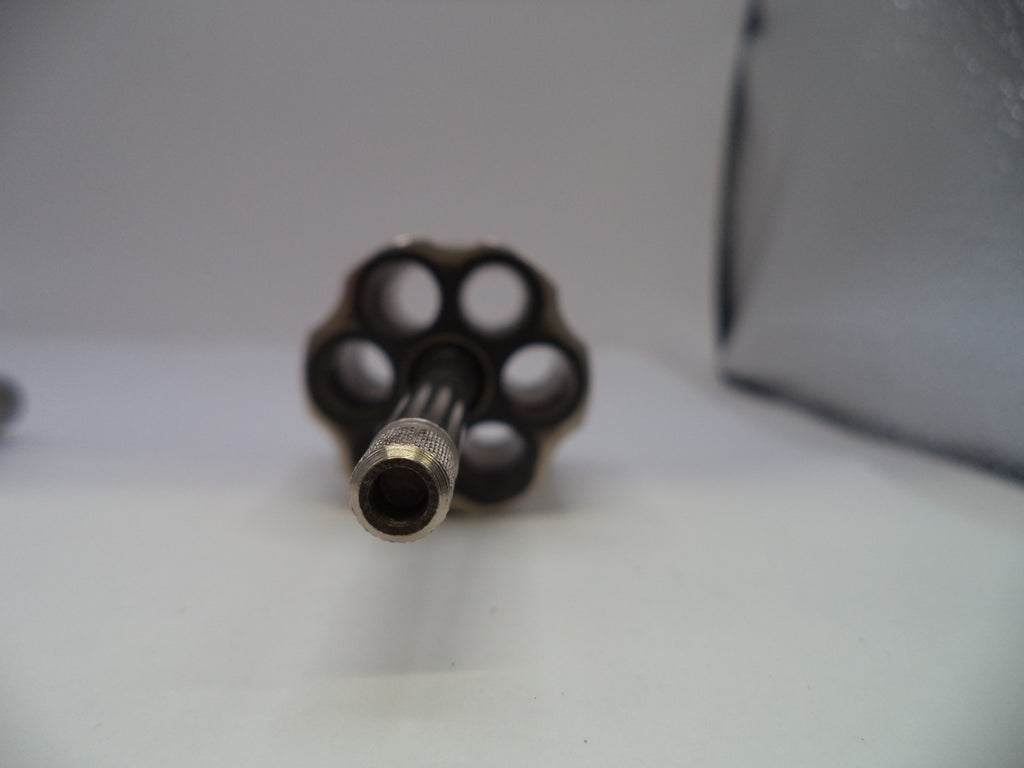 A close-up shot of a revolver's six-cylinder magazine and barrel, showing the metallic details and empty chambers, set against a plain light gray background.