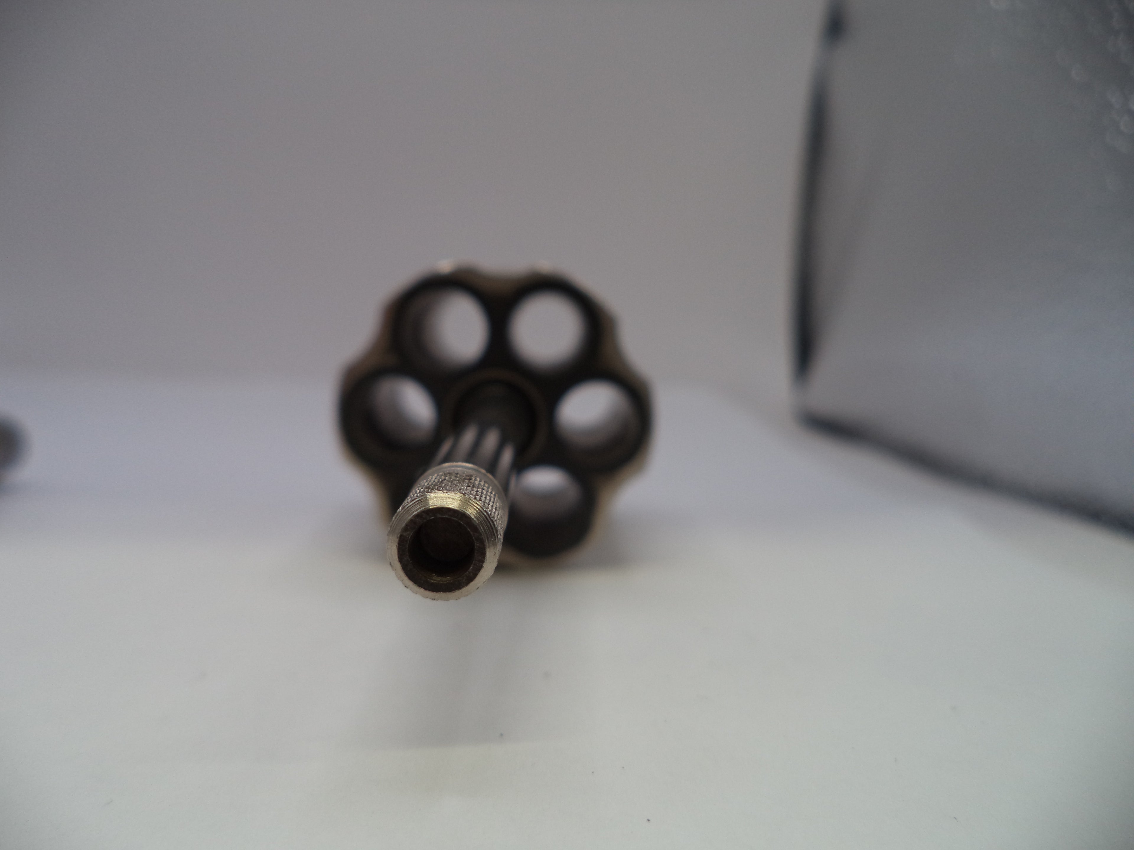 A close-up shot of a revolver's six-cylinder magazine and barrel, showing the metallic details and empty chambers, set against a plain light gray background.