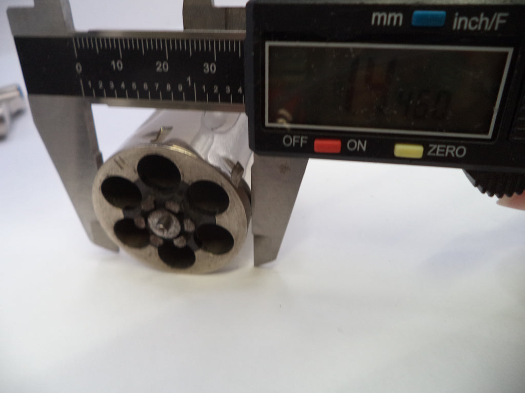 A close-up of a metallic cylindrical component with six circular openings, positioned under a digital caliper showing measurements in millimeters and inches.