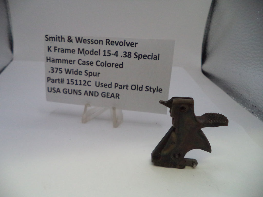 A used metal hammer case part for a Smith & Wesson revolver, displayed next to a white label card on a clear stand against a white background.