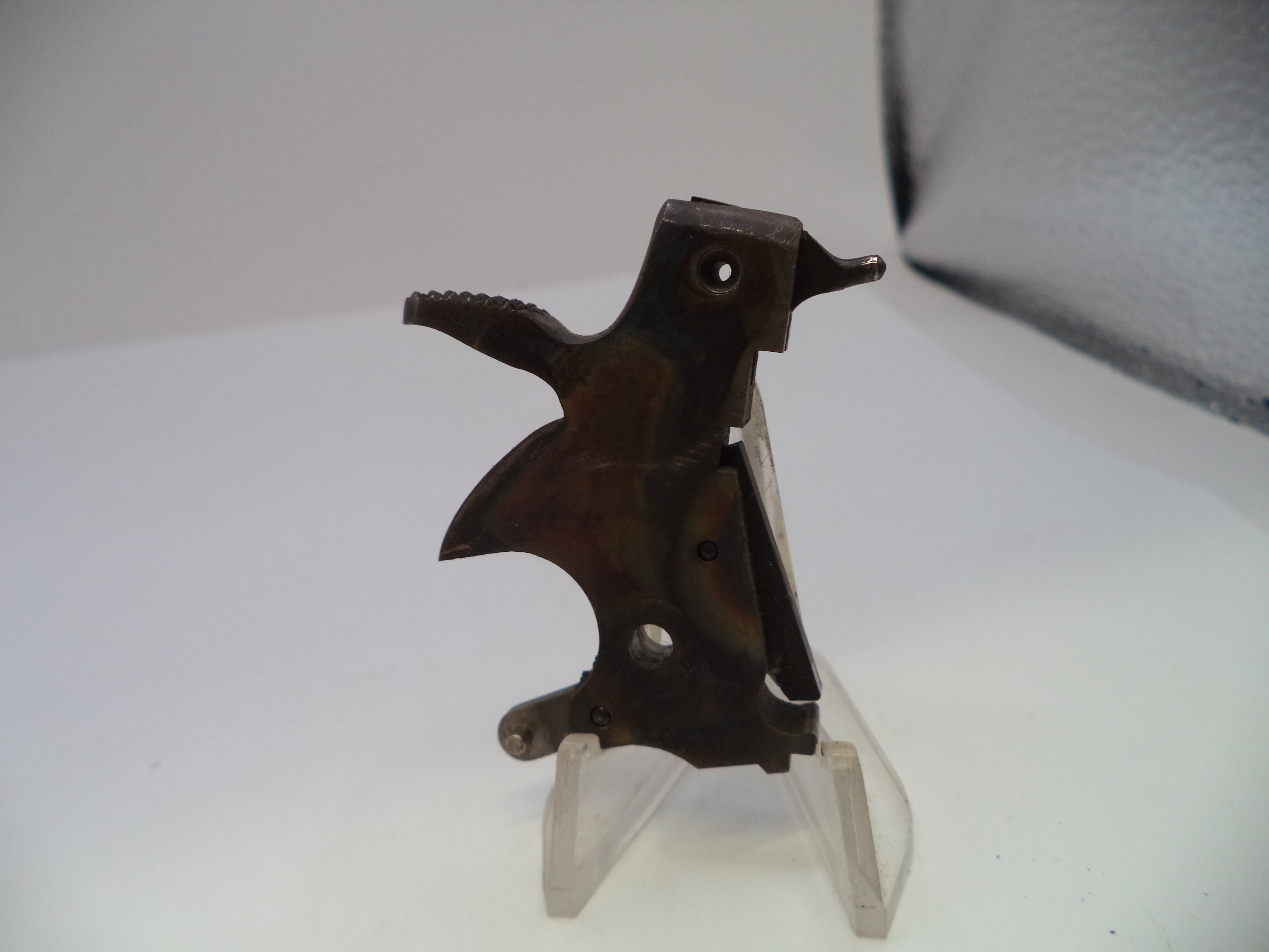 A small dark metal bird-shaped object displayed on a clear plastic stand against a plain light background.