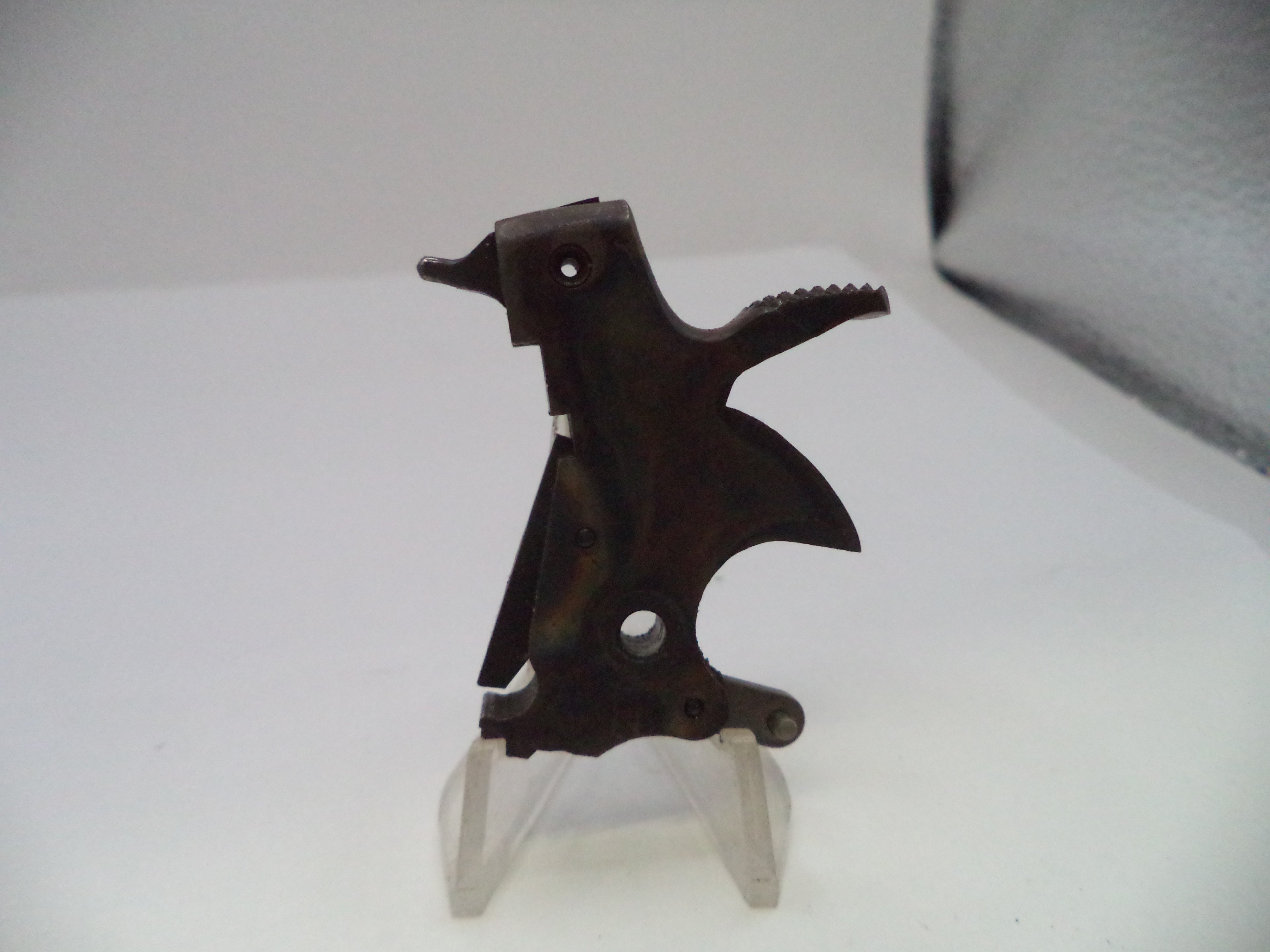 A dark metal firearm accessory or receiver component displayed on a clear plastic stand against a plain white background.