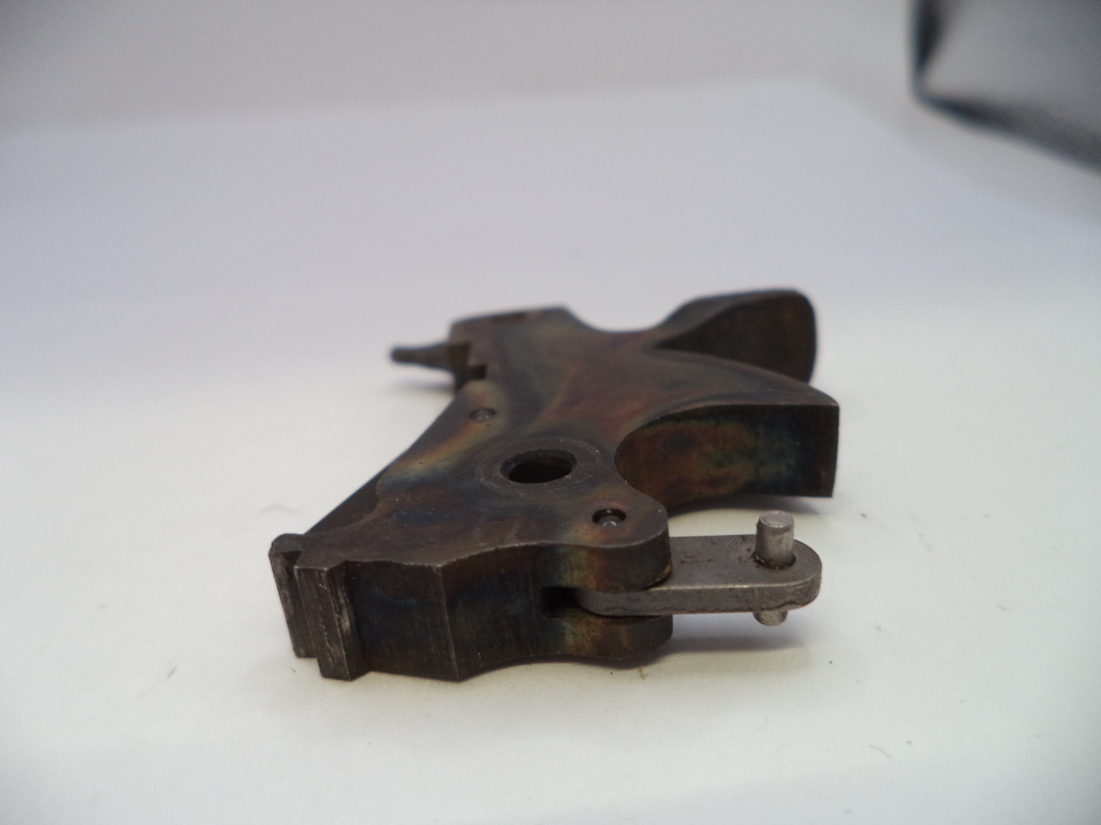 A dark brown and black metal gun stock or receiver component with a weathered, oxidized finish, resting on a plain white surface.