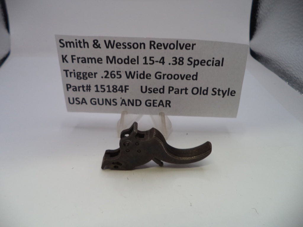 A small dark metal Smith & Wesson revolver trigger part displayed on a clear stand in front of a white label card with printed product details.