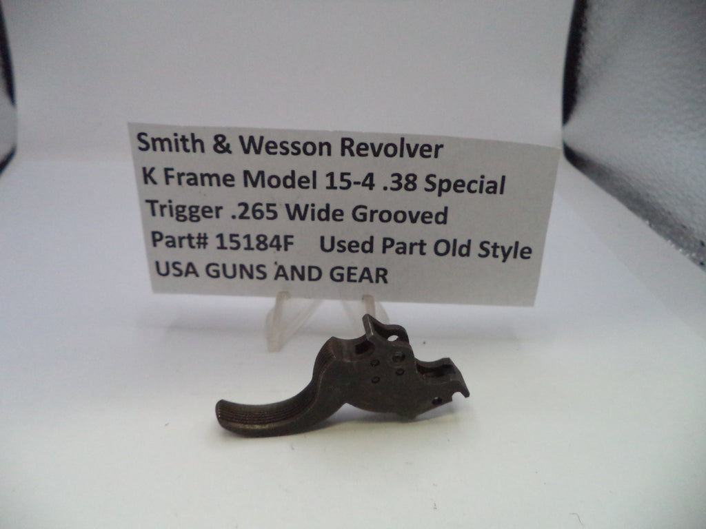 A used metal trigger component for a Smith & Wesson revolver, displayed on a white surface with a paper label card behind it.